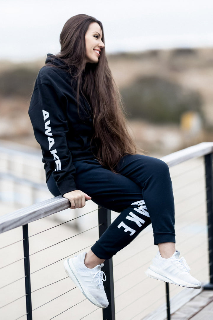 Beckah Shae wearing a black Awake Lion hoodie, sitting on a railing.