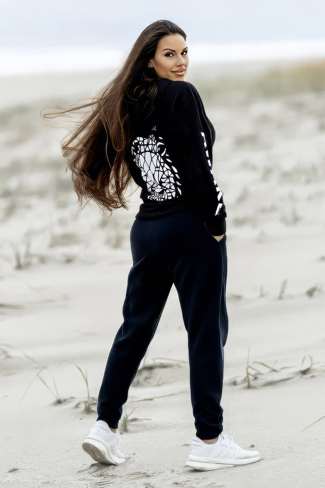Beckah Shae in a black Awake Lion Hoodie and black sweats with white lion design on a sandy beach