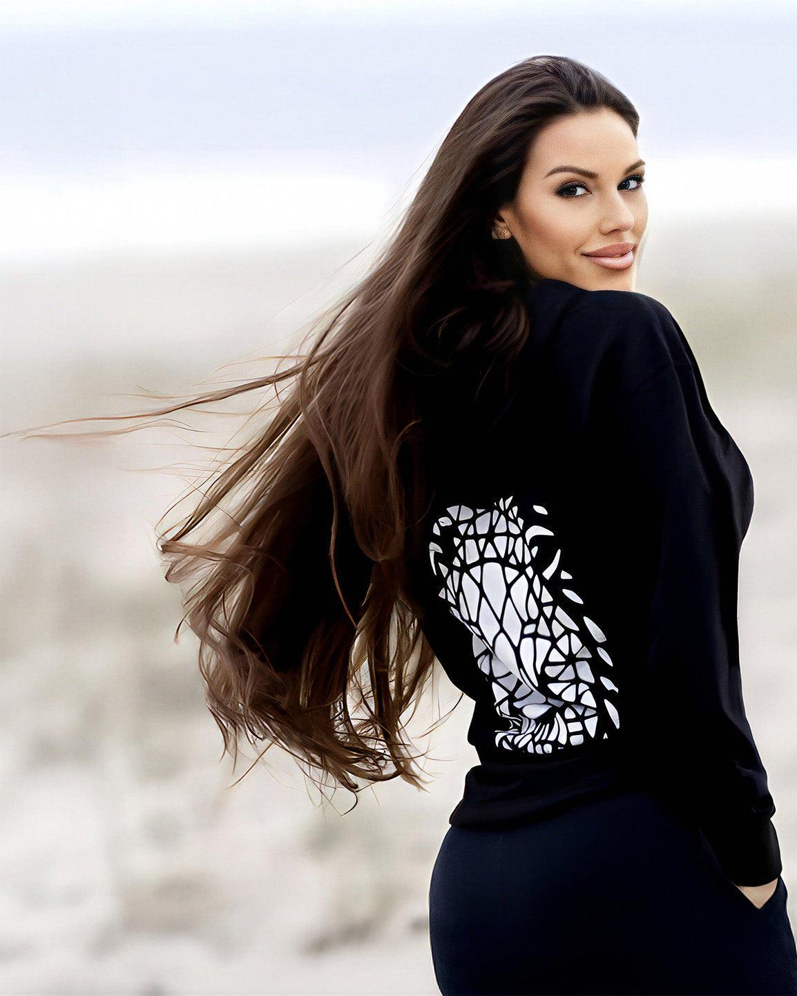 Beckah Shae standing on a beach wearing an Awake Hoodie with a blurred background