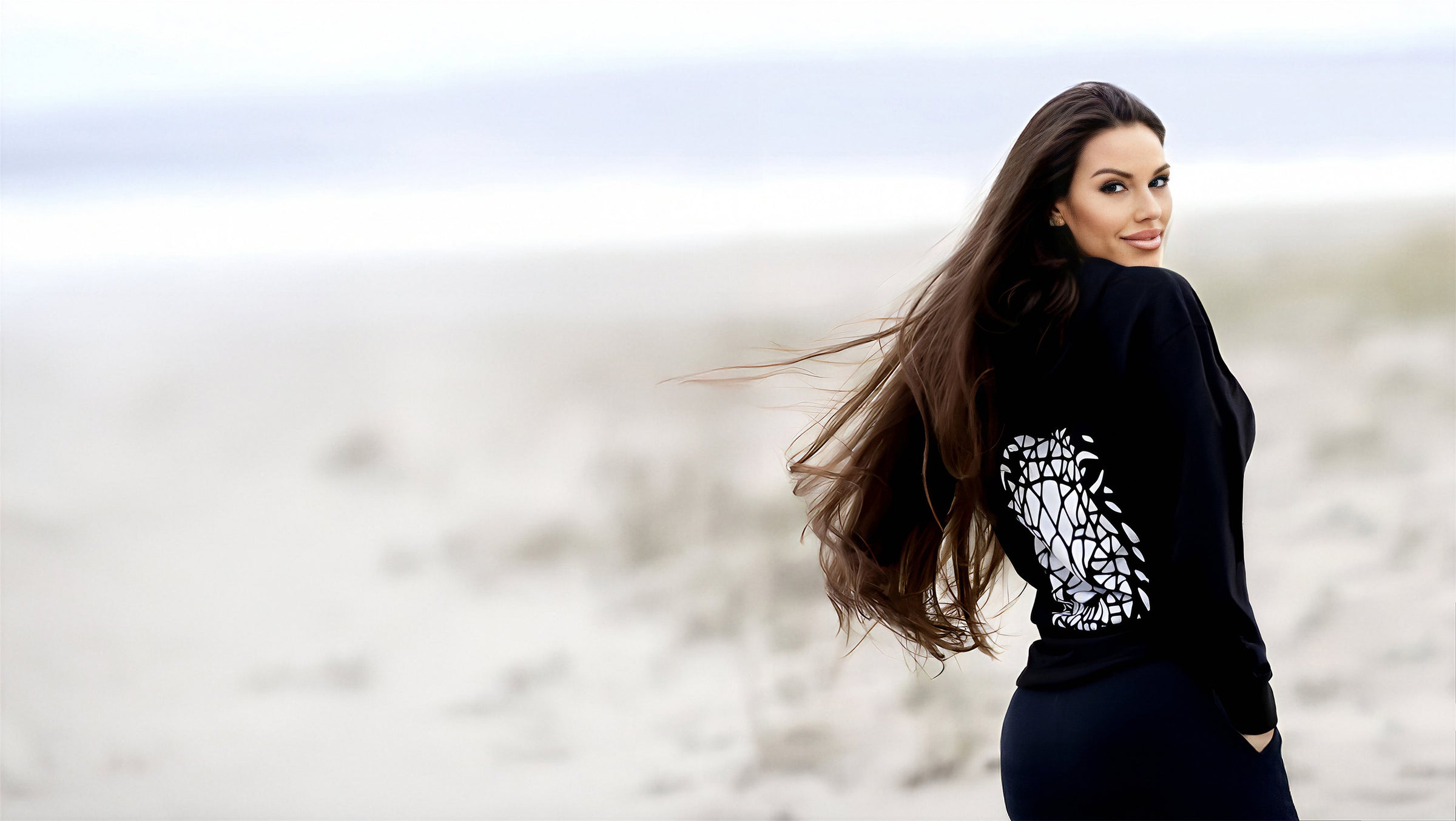 Beckah Shae standing on a beach wearing an Awake Hoodie with a blurred background
